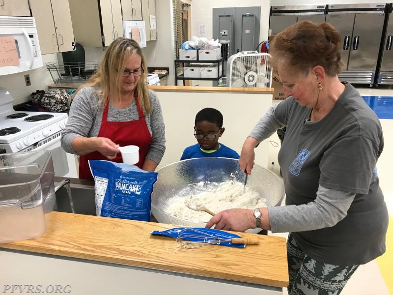 Members young and old preparing pancake mix.